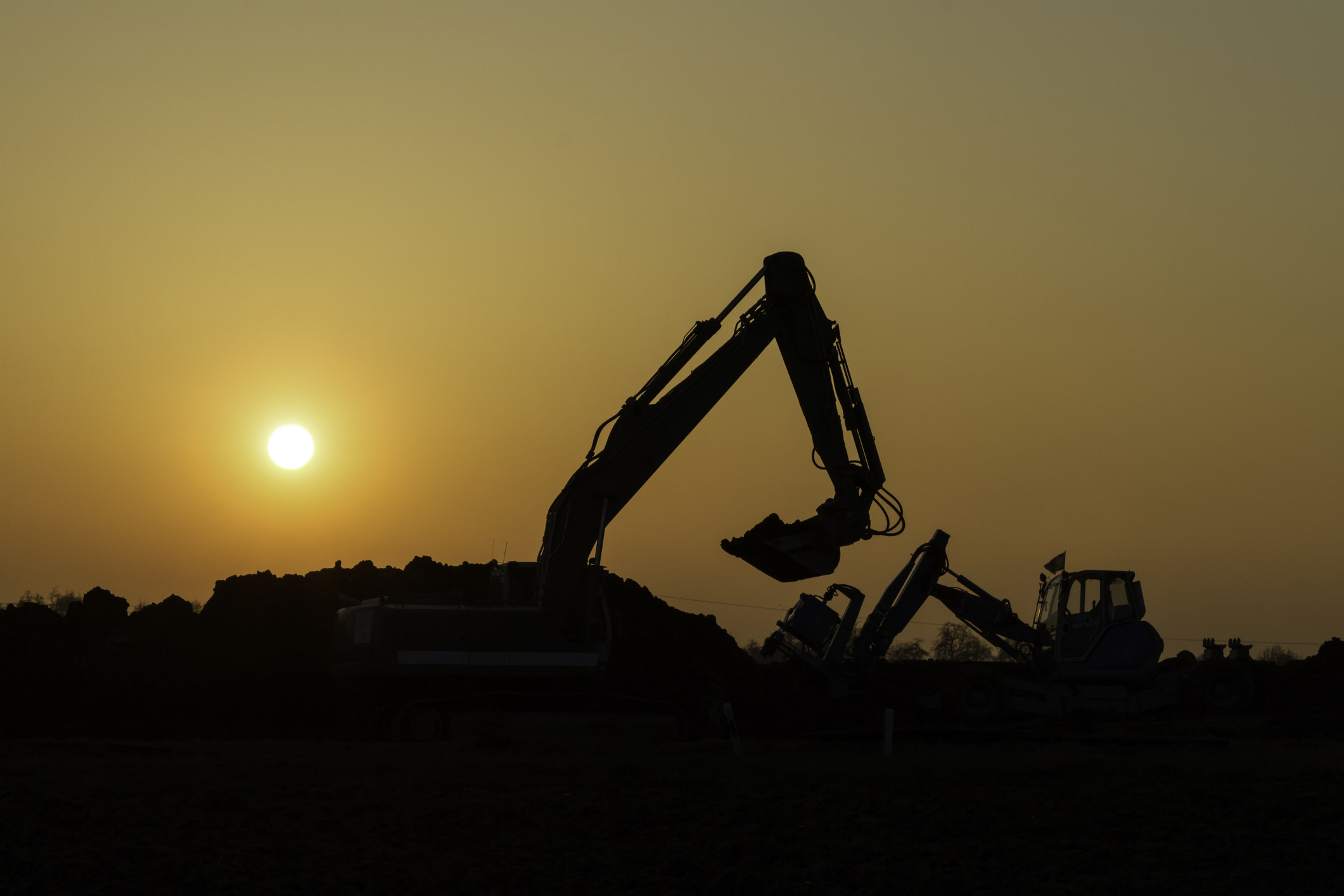 You see the black silhouettes of construction vehicles in the sunset